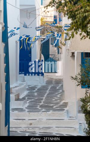 Washed white narrow streets, surrounded by lash blue colored windows and doors with the Greek flag in Mykonos, Greek island Stock Photo