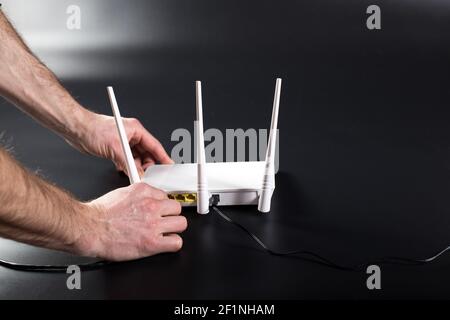 Hands connecting white wifi router with cable on black background. Stock Photo