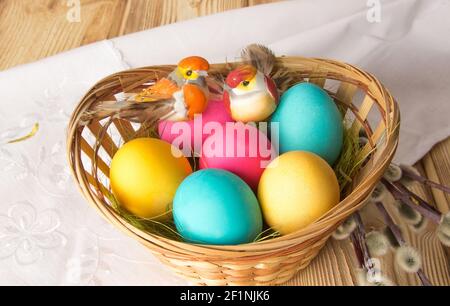 Two toy birds are hatching painted Easter eggs in a wicker plate. Stock Photo