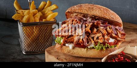 Appetizing pulled pork burger and French fries placed on wooden table with ketchup in cafe Stock Photo