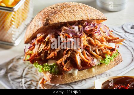 Closeup of yummy pulled pork burger served on table with French fries and sauce in cafe Stock Photo