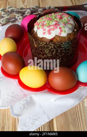 Close-up of a glazed Easter cake on a red plate with colored eggs . Stock Photo