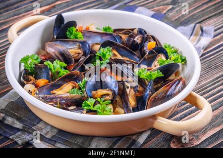 Boiled mussels in cooking dish with parsley on a wooden background