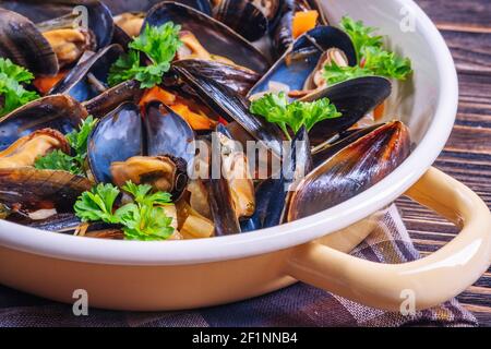 Boiled mussels in cooking dish with parsley on a wooden background