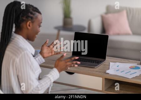 Back view of african american lady employee having online conference with her business team from home, looking at computer with blank screen, talking Stock Photo