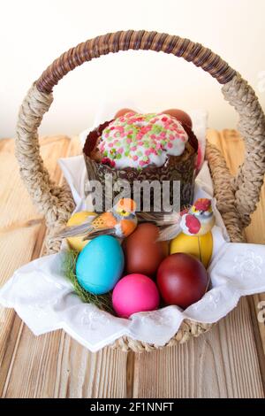 An Easter basket with a toy bird sitting on brightly colored eggs and a cake . Stock Photo