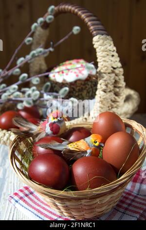 Toy birds sit in a wicker basket on painted eggs. In the focus of the cake and willow branches. Stock Photo