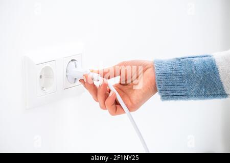 Hand plugging wire into socket on white wall Stock Photo