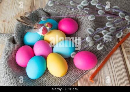 Bright colored Easter eggs lie on a natural wooden background, along with a toy bird and willow branches . Stock Photo