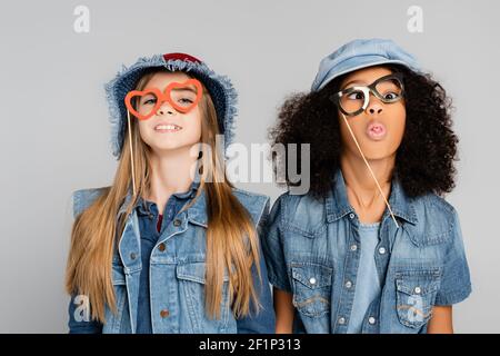 cheerful african american girl sticking out tongue while wearing party eyeglasses with friend isolated on grey Stock Photo