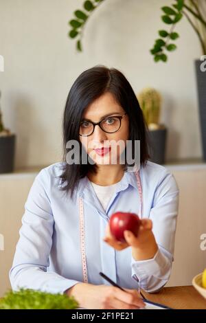 Nutritionist, dietitian woman at the office, hold apple in the hand, healthy vegetables and fruits, healthcare and diet concept. Female nutritionist w Stock Photo