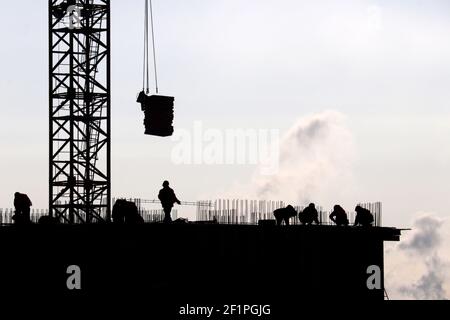 Silhouettes of workers and construction crane with cargo against the sky. Housing construction, builders working on scaffolding Stock Photo