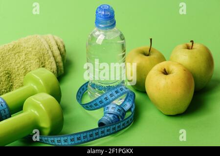 Barbells near juicy green apples. Healthy lifestyle equipment, close up. Diet and sport regime concept. Dumbbells in bright green color, water bottle, measure tape, towel and fruit on green background Stock Photo