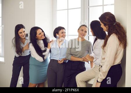 Business women chatting and joking in the office by the window while taking a break from work. Stock Photo