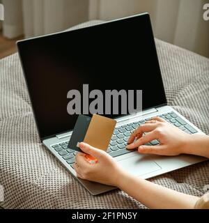 Female hands with cards blank mock up display laptop. Woman shopper makes online purchases using laptop and credit debit cards while sitting on couch Stock Photo