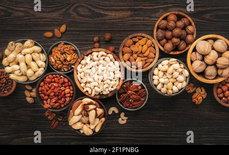 Assortment of nuts in bowls. Cashews, hazelnuts, walnuts, pistachios, pecans, pine nuts, peanuts, macadamia, almonds, brazil nuts. Food mix on wooden Stock Photo