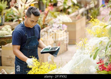 Handsome young Asian man wearing gloves when working with plants in greenhouse Stock Photo