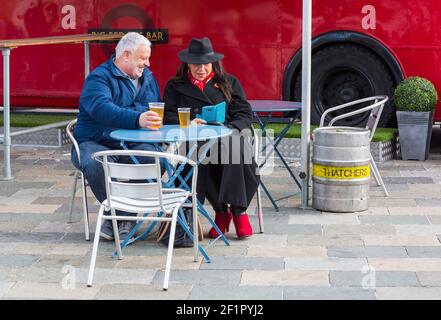 Couple looking at mobile phone, enjoying a rest and drinks at Gloucester Quays Victorian Christmas Market, Gloucester, Gloucestershire in November. Stock Photo
