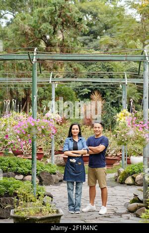 Cheerful young Vietnamese flower nursery workers folding arms and smiling at camera Stock Photo