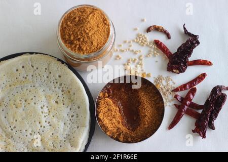 Indian pancakes are also known as dosa made with a fermented batter of rice and lentils. Served with idli podi chutney, sambar, coconut chutney and a glass Stock Photo