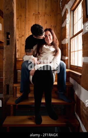 Attractive couple sitting on stairs together inside rustic log cabin. Stock Photo