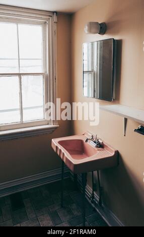 Retro vintage pink sink an mirror in an old empty dingy bathroom. Stock Photo