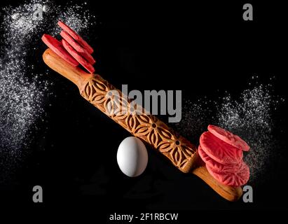 https://l450v.alamy.com/450v/2f1rbcw/red-sable-breton-cookies-in-a-balancing-design-with-a-rolling-pin-and-an-egg-creative-home-baking-concept-on-black-background-copy-space-2f1rbcw.jpg