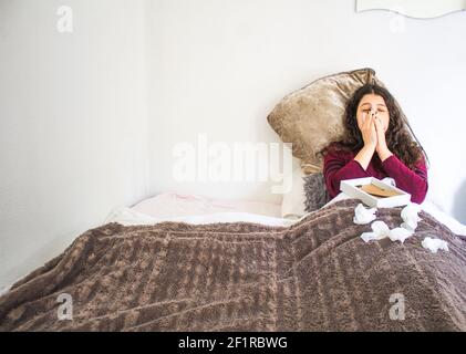 young woman lying crying with photograph and handkerchiefs in bed Stock Photo