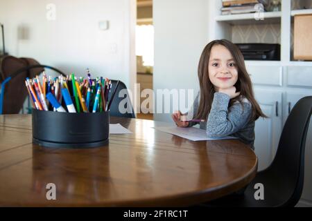 Little Girl Sitting at a table with paper and pencil. Stock Photo