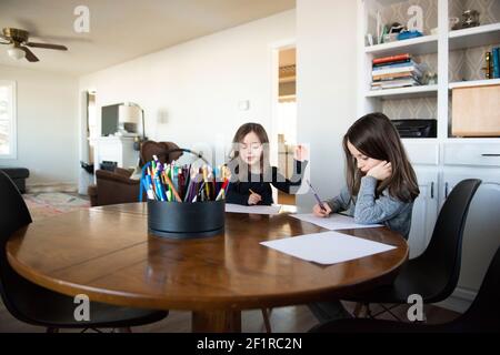 Two young girls at a table doing schoolwork. Stock Photo