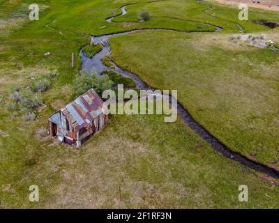 Aerial view of abandoned little wooden house barn next small river in the green valley, Aspen Spring Stock Photo
