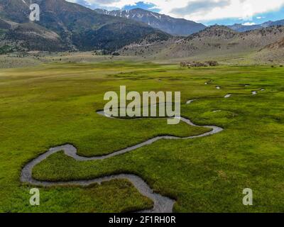 Aerial view of green land and small curve river with mountain in the background in Aspen Springs