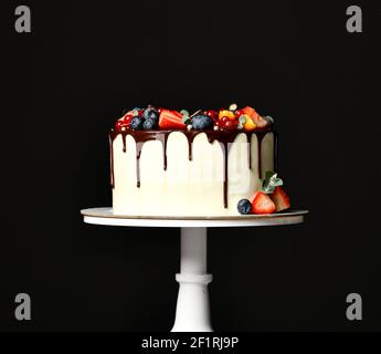 Birthday sweet cake with chocolate drips and fresh fruits Raspberry strawberry blueberry cranberry on dark black Stock Photo