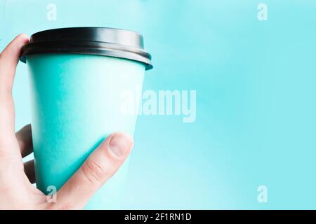 Woman’s hand holds a takeaway coffee cup over blue background. Copy space for the text Stock Photo