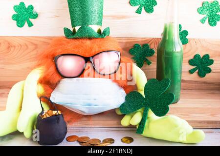 Corona Patrick’s Day. Toy leprechaun with ginger beard in face medical mask and sunglasses. Saint Patrrick’s Day celebration during the coronavirus pa Stock Photo