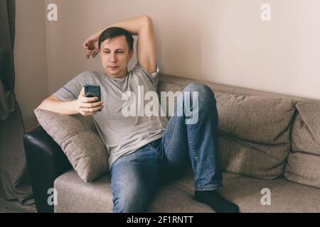 Serious man having rest using smartphone sitting on sofa at home Stock Photo