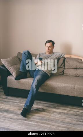 Serious man having rest using smartphone sitting on sofa at home Stock Photo