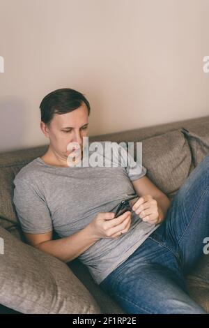 Serious man having rest using smartphone sitting on sofa at home Stock Photo