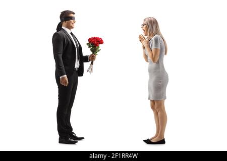 Full length profile shot of a man in a suit with blindfold giving a bunch of red roses to an excited young woman isolated on white background Stock Photo