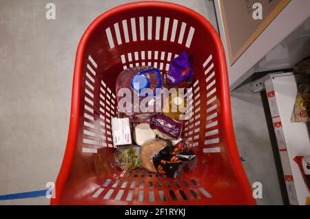 Mar del Plata, Buenos Aires, Argentina - June, 2020: Small red plastic supermarket cart with basic products like water in bottle, sunflower oil, bread Stock Photo