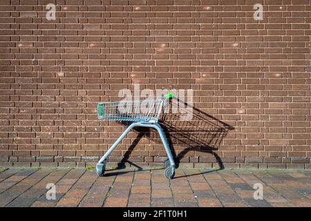 abandoned, empty supermarket trolley by a brick wall, shopping concept. Stock Photo