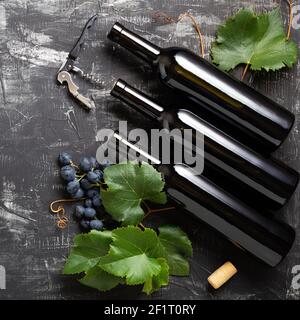 Wine bottles grapes, grape bunches with leaves and vines corkscrew wine corks on dark rustic concrete background. Wine composition on black stone tabl Stock Photo