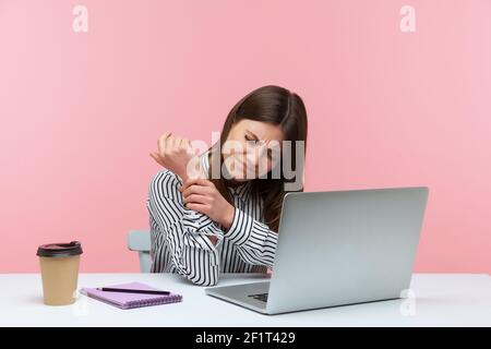 Unhappy sad woman office worker feeling pain in her wrist working on laptop sitting at workplace, suffering joint inflammation, rheumatoid arthritis. Stock Photo