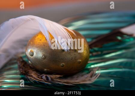 golden egg with plume on a glass plate Stock Photo
