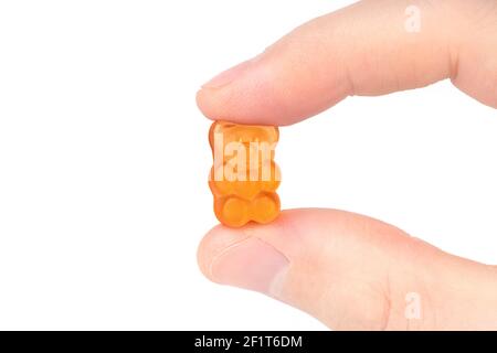 Crop view of male fingers holding an orange gummy bear against white background. Stock Photo