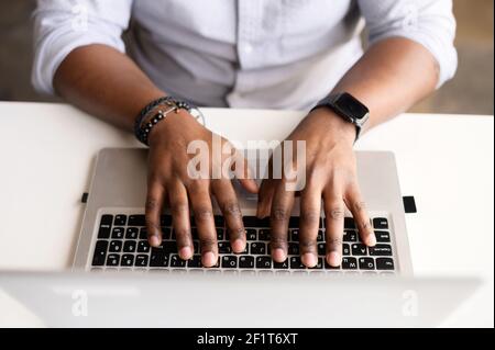 A male hands on the laptop keyboard. Top view an African-American guy is typing email, programmer is develops software, cropped photo, a face is not visible, close-up picture Stock Photo