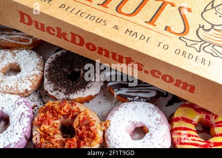 Clarksburg, MD, USA 03-04-2021: A cardboard box of a dozen donuts bought from the chain store Duck Donuts. A popular selection of assorted donuts are Stock Photo