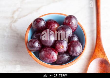 A simple image of a porcelain bowl or red grapes  and a wooden spoon on marble countertop. A concept image for vegan, raw healthy eating. Stock Photo