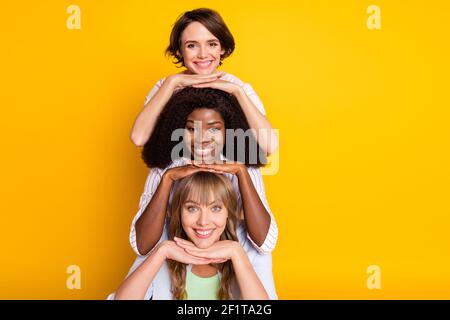 Portrait of three attractive cheerful girls standing in hierarchy isolated over bright yellow color background Stock Photo