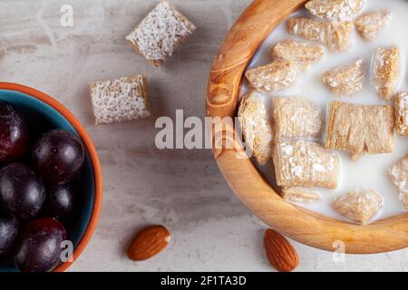 A simple breakfast concept with a bowl of frosted bite size wheat cereal in milk on marble kitchen countertop. There are grapes and nuts as appetizers Stock Photo
